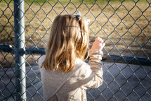 On the other side of the fence - child looking through a chain link fence onto a closed playground