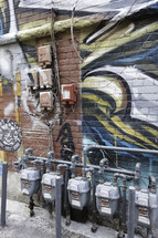 utility boxes and gas meters and graffiti on a wall 
