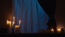 Static shot of a window sill with burning candles, scrolls, and moonlight coming through the window.