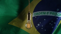 Flickering classic antique Edison Tungsten filament lamp on waving brazilian flag background. Raising tariffs for electricity supply, bills, energy crisis in Brazil, South America. High quality 4k