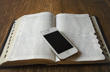 cellphone on the pages of an open Bible on a wood floor 
