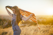 a young woman carrying an American flag in a field at sunset 