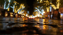 People Walking On Rainy Cobbles European Well Illuminated Street. City Life