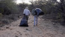 Men hauling bags of trash left in the desert by illegal immigrants