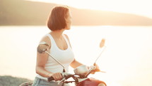 Woman Sitting On Red Retro Motor Bicycle At Sunset River