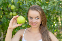 a young woman holding up a green apple 