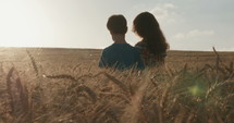 Young girl putting her around around a young boy in a wheat field with sunlight