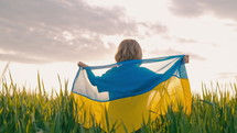 Happy little boy - Ukrainian patriot child with national flag in green field, open area. Ukraine, peace, independence, freedom, win in war.