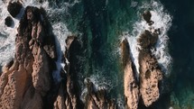 Aerial top down view of ocean waves in turquoise water crashing on a rocky beach during sunset