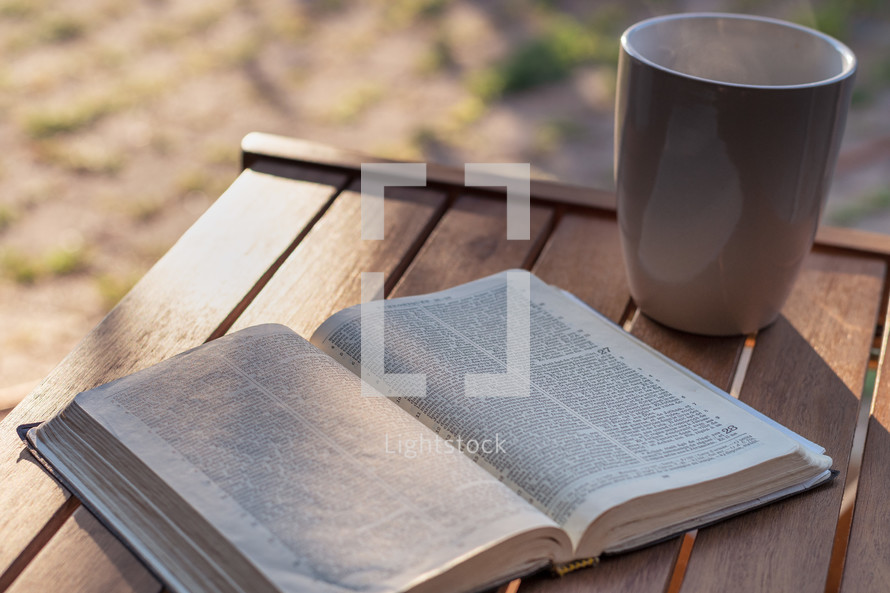 open Bible and coffee mug on an outdoor table 