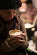 A woman in winter clothing holds a hot beverage.