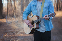 man standing outdoors holding an acoustic guitar 