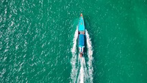 Wooden boat in turquoise sea, movement on blue water. Trip boat with tourists sailing on clean blue sea surface. A long-tailed Thai boat sails among the islands, touristic excursion ride. Aerial. 