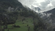 Aerial drone flying through the misty mountains with small chalet and homes on hillside