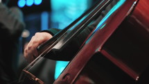 Close, full-frame detail on the hands, fingerboard and bowing technique of a professional cellist playing her instrument.