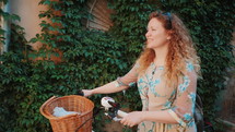 Portrait of beautiful young woman with blonde curly hair wearing retro style dress standing on lush foliage background with vintage white bicycle. Slow Motion.