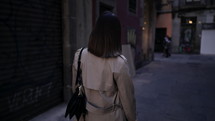 Back view of woman walking alone in Barcelona Gothic Quarter. Old apartment buildings, narrow streets of Europe. Traveling in autumn, lady in trench coat.