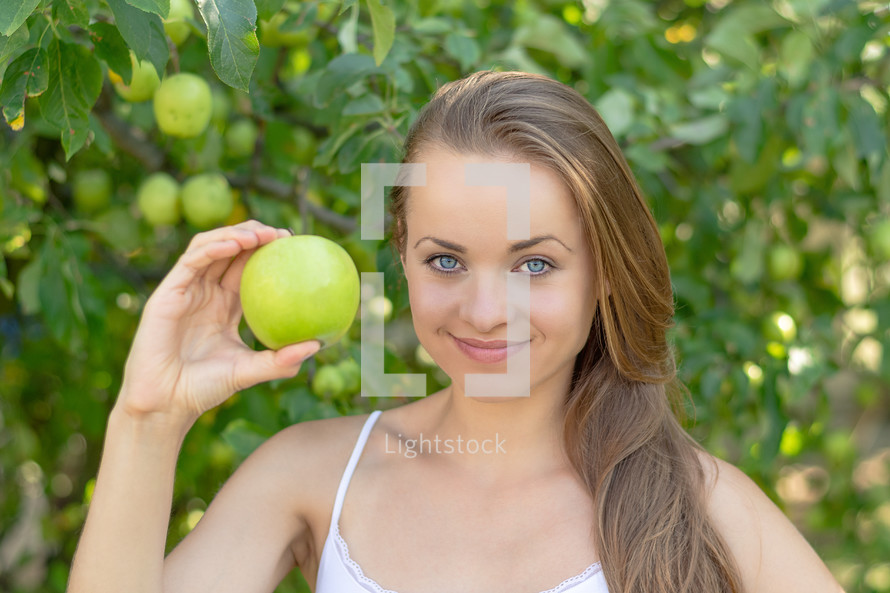 a young woman holding up a green apple 