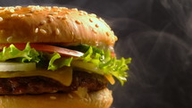 Yummy fast food concept. Fresh homemade grilled burger with meat patty, tomatoes, cucumber, lettuce, onion and sesame seeds. 