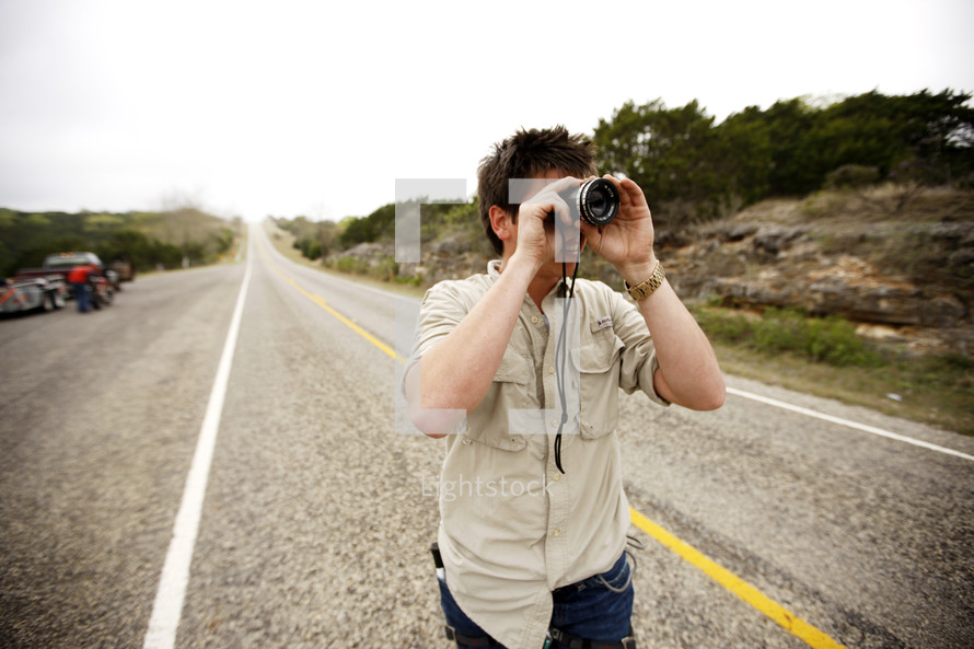A man looking through a lens on a highway road