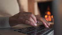 Business woman working on laptop, sitting near cozy fireplace at home. Focus on hands typing on keyboard. Social distancing, creative workspace concept. Lady shopping online through website.4k footage