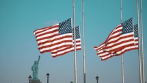 statue of Liberty and American flags on flagpoles at half staff 