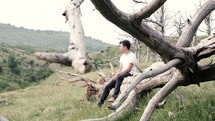 young man sitting outdoors on a fallen tree 