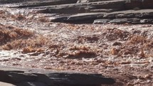 Follow muddy flooded river splashing in rapids after heavy rain storm slow motion
