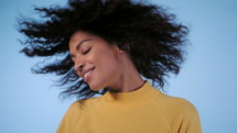 Beautiful African American woman with curly hair having fun smiling and dancing in studio against blue background. slow motion
