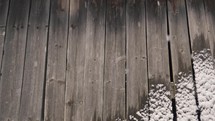 Snow falling on an old wooden wall made of gray planks with snow.
