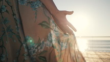 The hand of a young girl standing on the embankment near the sea and looking at the rising sun. Lady Energized by the sun, freedom concept. Windy weather.