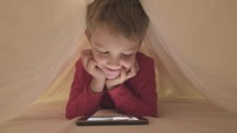 a child watching a movie on a tablet under the covers 