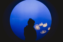 silhouette of a woman looking at jellyfish at an aquarium 