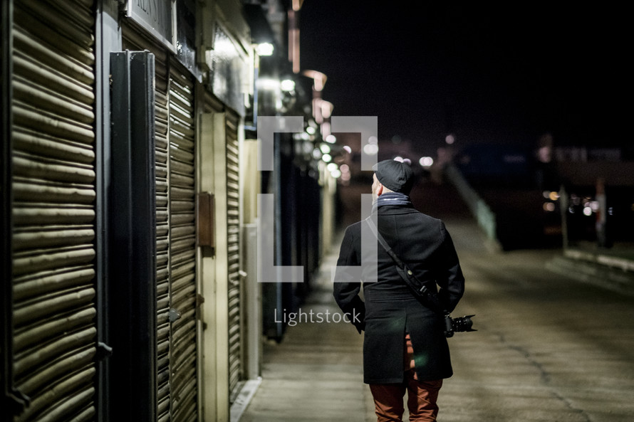 man with a camera walking on a sidewalk at night 