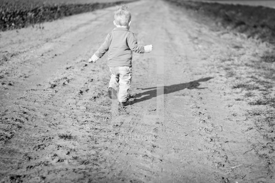 toddler boy running on a dirt road 