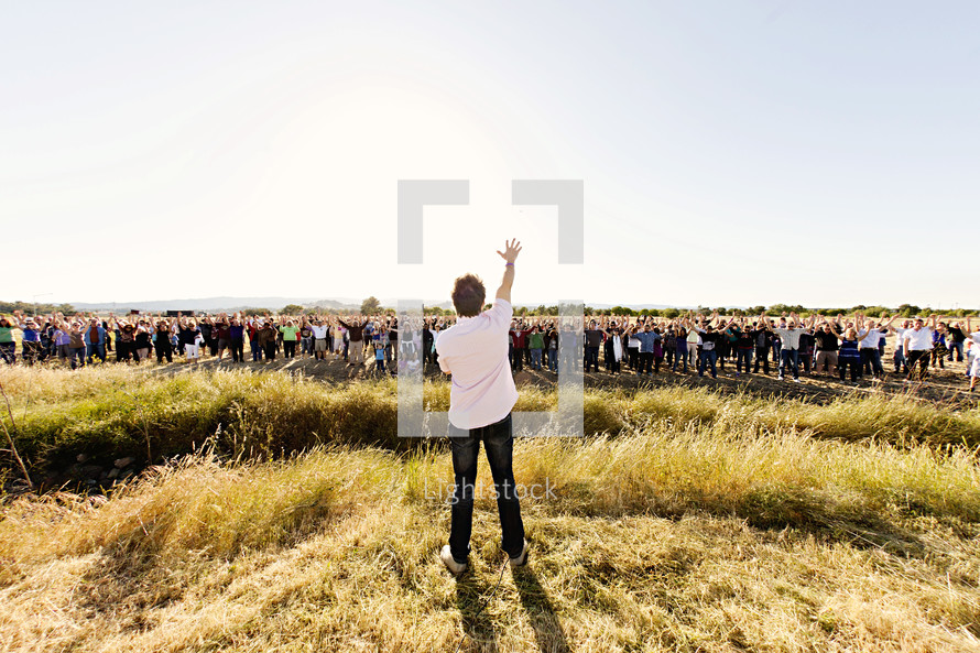 A man speaking to a crowd of people in a field, with his arm raised prayer proclamation land  leadership, new beginnings, church construction, pray on the property, new land.