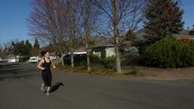 A young woman jogging down a residential street.
