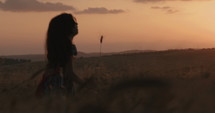 young girl in a golden field during sunset raising her hands in happiness