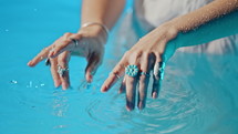 Woman in water imitates playing music on piano. Boho jewelry, rings with stones on fingers. Girl in white dress swimming in pool or lake. Femininity, trend, hippie style concept. High quality 4k