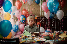 A 6-year-old child sits in a messy room after their birthday celebration. Deflating balloons, scattered gifts, and a slightly sad expression