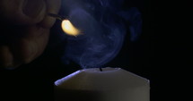 Slow motion macro footage of a white candle lit by a match on a dark background