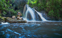 Tourist man with backpack sit and relax at the waterfall