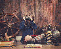 a little girl holding a camera and a nautical travel scene 