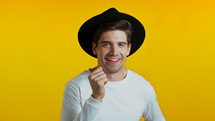 Happy european hipster man dancing, showing yeah gesture of victory, he achieved result, goals. Surprised excited guy in hat on yellow background. High quality 4k footage