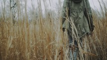 a woman walking through a field of tall brown grasses 