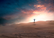 silhouette of a man with outstretched arms on sand dunes 