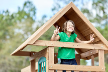 child in a playhouse giving peace signs 