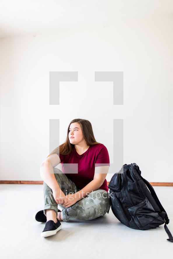 teen girl sitting next to a book bag 