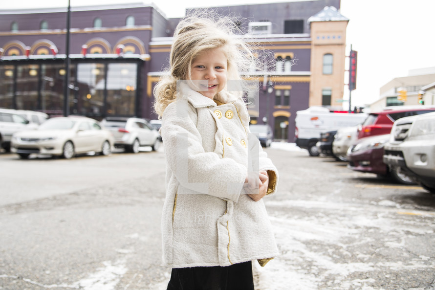 a smiling girl in a coat in a parking lot 