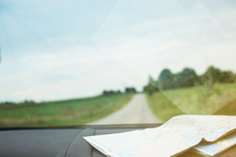 A road map on the dashboard of a car with a country road in front.